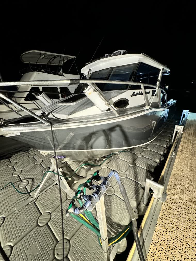 Boat docked on a floating dock attached to metal docking equipment attached to the pier at night.