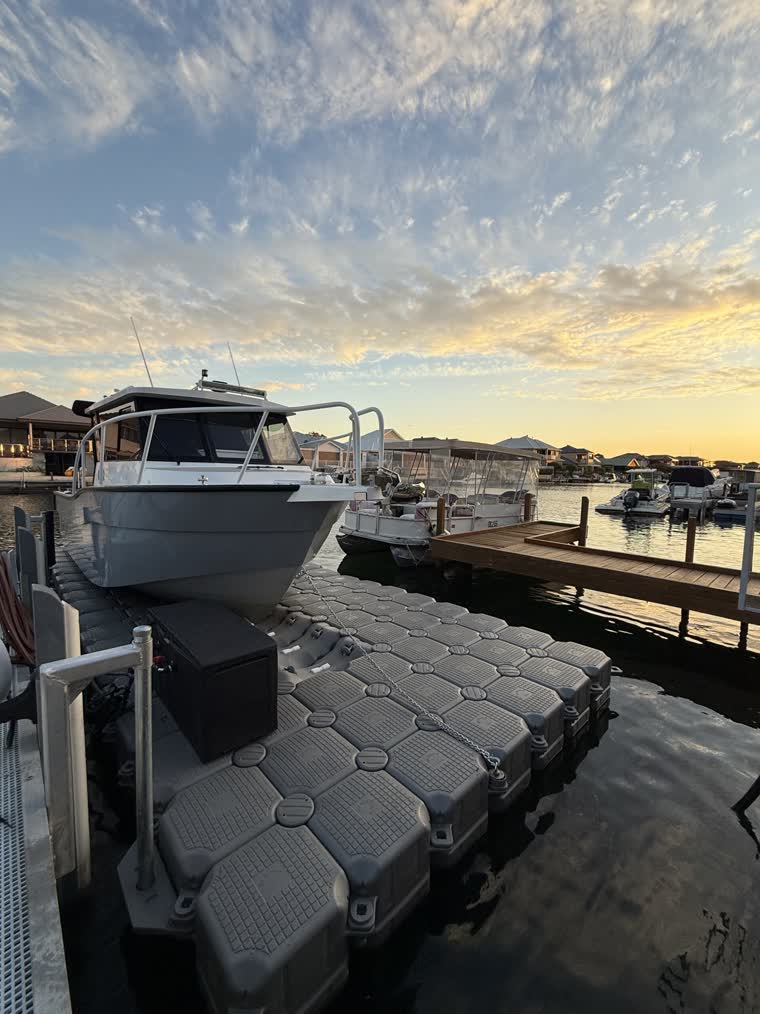 Front view of a boat on a partly cloudy day as the sun sets, other docked boats are visible