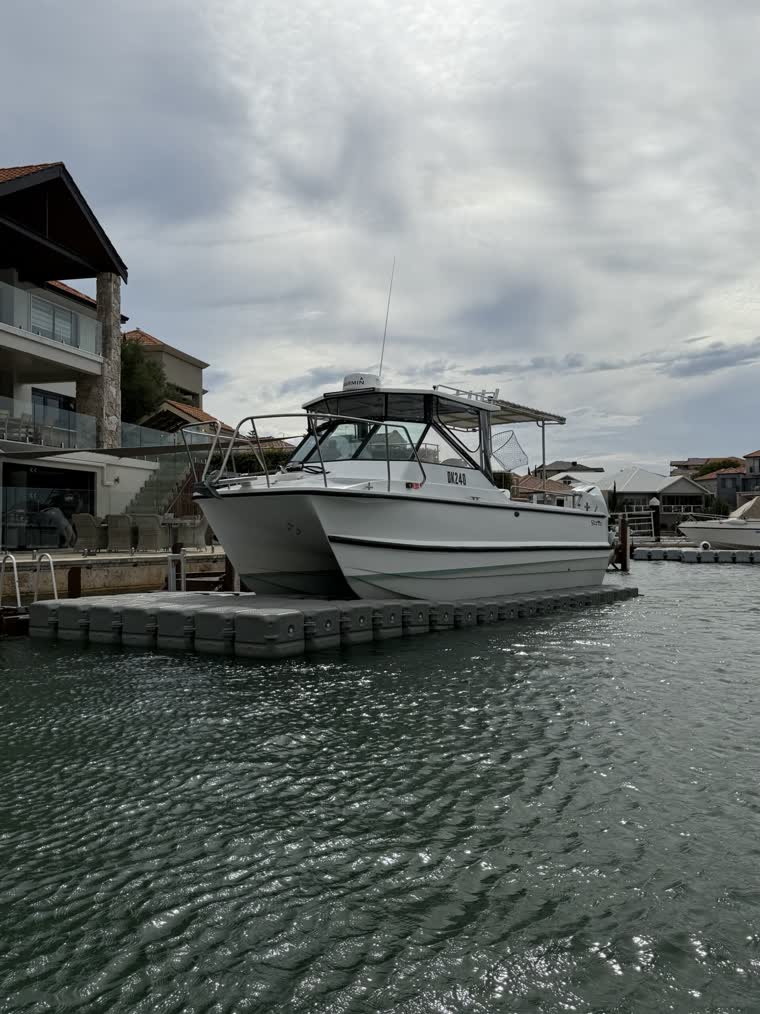 A large catamaran boat on a dock in front of a house on a cloudy day
