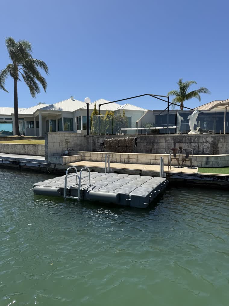 Swim platform dock on a sunny day in front of a house with two chairs behind the dock