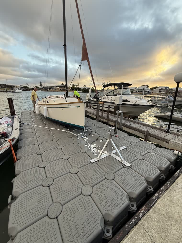 2 people putting a white boat on a floating dock with visible ropes and docking materials
